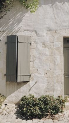 an old building with shutters on the windows and plants growing in front of it