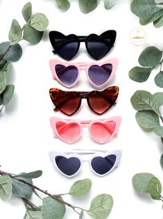 four pairs of heart shaped sunglasses sitting on top of leaves