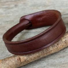 a brown leather bracelet sitting on top of a piece of wood next to a wooden stick