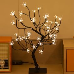 a lighted tree with white flowers is on a table next to an old fashioned radio