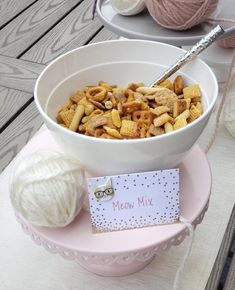 a bowl filled with cereal sitting on top of a pink plate next to a ball of yarn