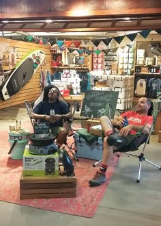 two men sitting in chairs with surfboards on the wall and other items behind them