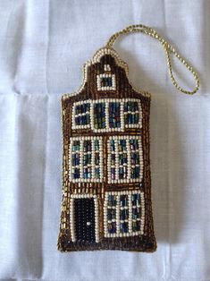 a beaded house ornament hanging on a white tablecloth with a gold chain