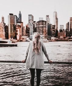 a woman standing on the edge of a bridge with her back to the camera