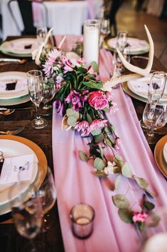 the table is set with pink flowers and deer antlers