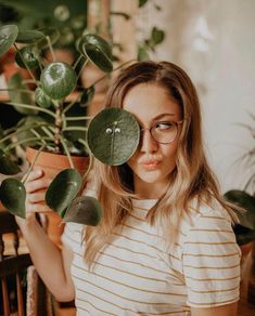 a woman holding up a potted plant with eyes drawn on it