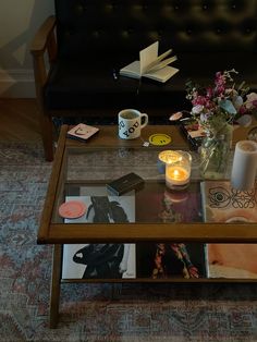 a coffee table with magazines, candles and flowers sitting on the floor next to a couch