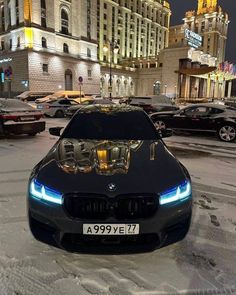 a black car parked in the middle of a snow covered parking lot next to tall buildings