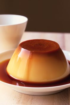 a caramel pudding on a white plate next to a cup