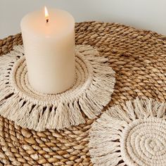 a white candle sitting on top of a wicker table mat with two small tassels