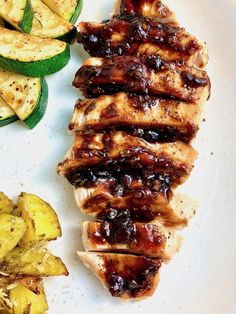 a white plate topped with meat covered in bbq sauce next to sliced zucchini