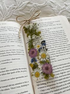 an open book with flowers on it and a string tied to the page in front of it