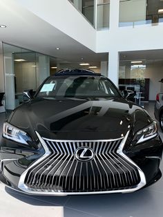 a black car is parked in a showroom with other cars and people looking at it