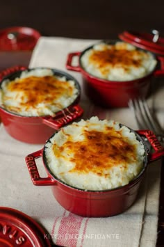 three red dishes filled with mashed potatoes sitting on top of a table next to silverware