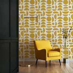 a yellow chair sitting in front of a wall with a pattern on it and a lamp next to it