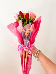 a hand holding a bouquet of roses with a barbie doll in it