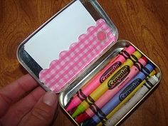 an open tin with crayons in it on top of a wooden table next to a person's hand