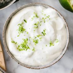 a bowl filled with sour cream next to limes