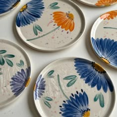 four plates with painted flowers on them sitting on a counter top next to each other