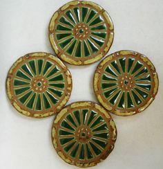 four green and gold decorative plates on a white surface