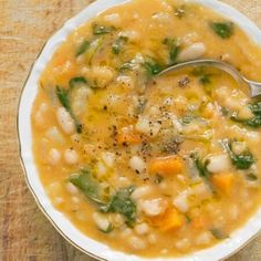 a white bowl filled with soup sitting on top of a wooden table next to a spoon