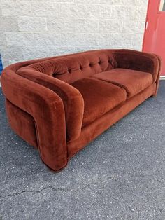 a brown couch sitting in front of a red door on the side of a building