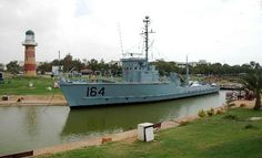 a large boat is docked in the water next to a light house and grassy area