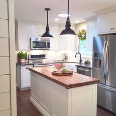 a kitchen with white cabinets and stainless steel appliances, including an island that has a cutting board on it