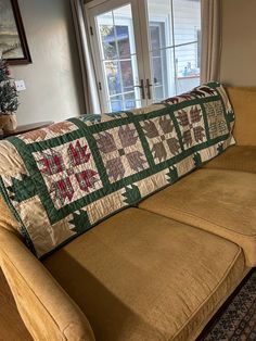 a couch with a quilt on it sitting in front of a window next to a rug