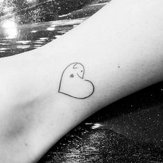 a small heart tattoo on the foot of a person's leg, with water in the background