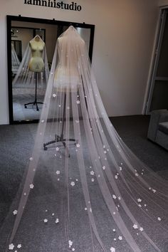 a wedding veil with white flowers on it in front of a dress mannequin