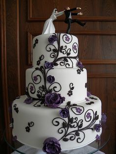 a wedding cake with purple flowers and a bride and groom figurine on top