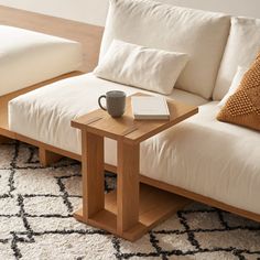 a wooden table with a book and cup on it next to a white couch in a living room