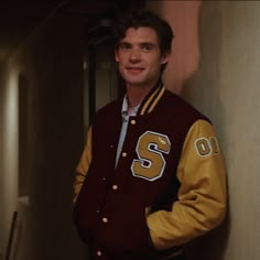 a young man in a maroon and gold jacket standing next to a wall with his hands on his hips