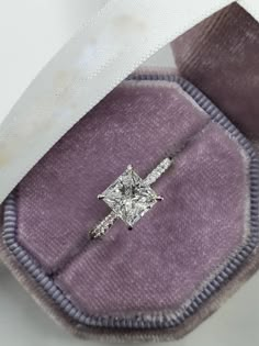 an engagement ring with a princess cut diamond sits in a velvet box on top of a label that says benzz & co