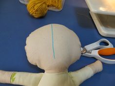 a doll is sitting on the table next to scissors and yarn