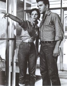 a man and woman standing next to each other in front of a glass wall pointing at something