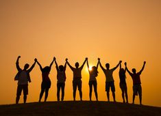 group of people standing on top of a hill with their arms in the air at sunset