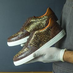 a person in white gloves is holding two brown shoes with leopard print on the soles