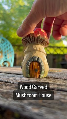 a hand is touching a mushroom house on a wooden table with trees in the background