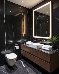 a modern bathroom with black marble walls and flooring, along with a large mirror above the sink