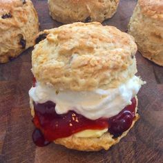 biscuits with jam, cream and jelly on them sitting on a cutting board next to other biscuits