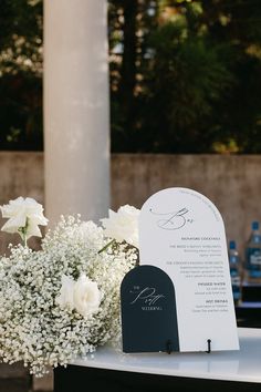 a table with white flowers and a sign on it next to a tall pillar in the background