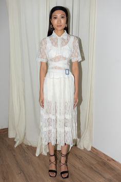 a woman standing in front of a curtain wearing a white dress with sheer lace on it