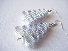 two silver earrings are sitting on a white tablecloth and one is made out of fabric