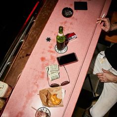 a man sitting at a pink table with food and drinks on it, next to his cell phone