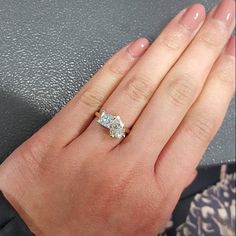 a woman's hand with a diamond ring on top of her left hand and the other hand holding an engagement ring