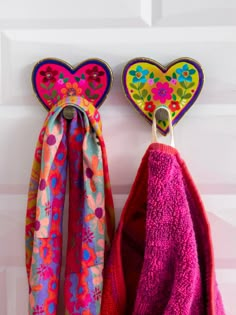 two colorful towels hanging from hooks on a white door with hearts and flowers painted on them