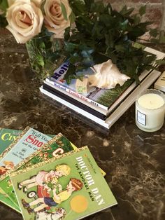 some books are sitting on a table next to a candle and flower vase with roses in it