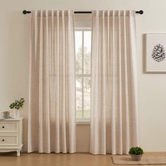 a living room with a white couch and two curtains on the window sill, next to a potted plant